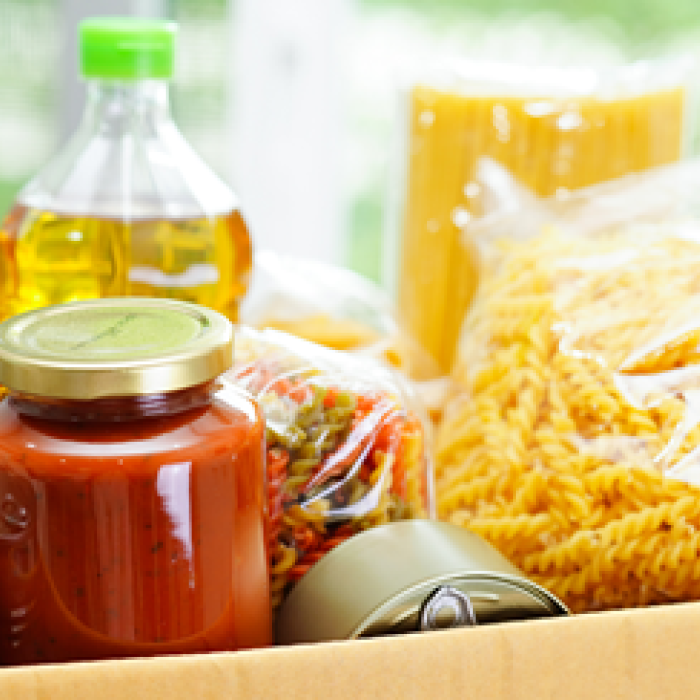 A box filled with packaged food items including pasta, canned goods, and bottles of oil.
