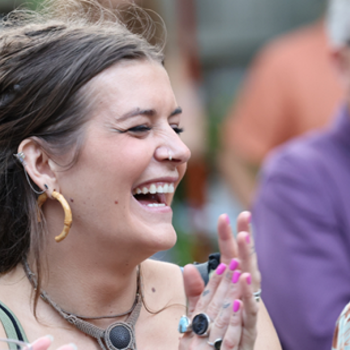 A woman laughing and clapping in a crowd at an outdoor event.
