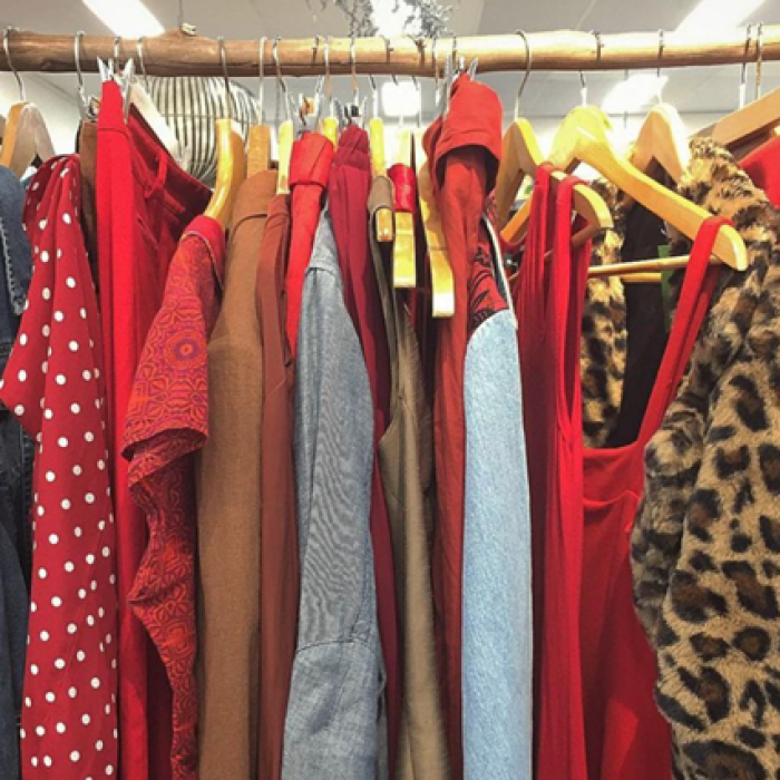 Clothing rack with red, brown, denim, and leopard-print garments hanging on wooden hangers.
