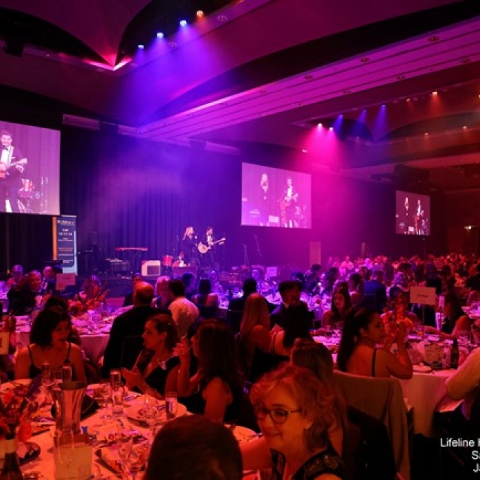 Guests seated at decorated tables during an indoor gala event with live music on stage.