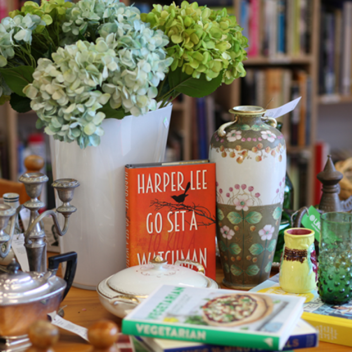 Assorted books, vases, and vintage homeware displayed on a wooden table with flowers.