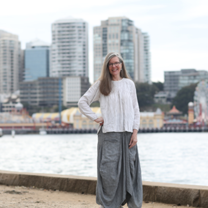 A woman standing and smiling by the waterfront with a city skyline behind her.