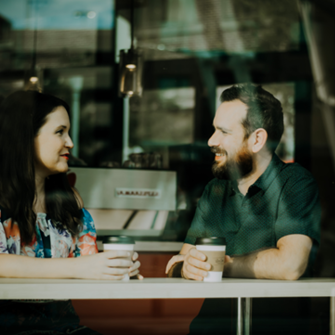 Two people sitting at a café table talking over coffee