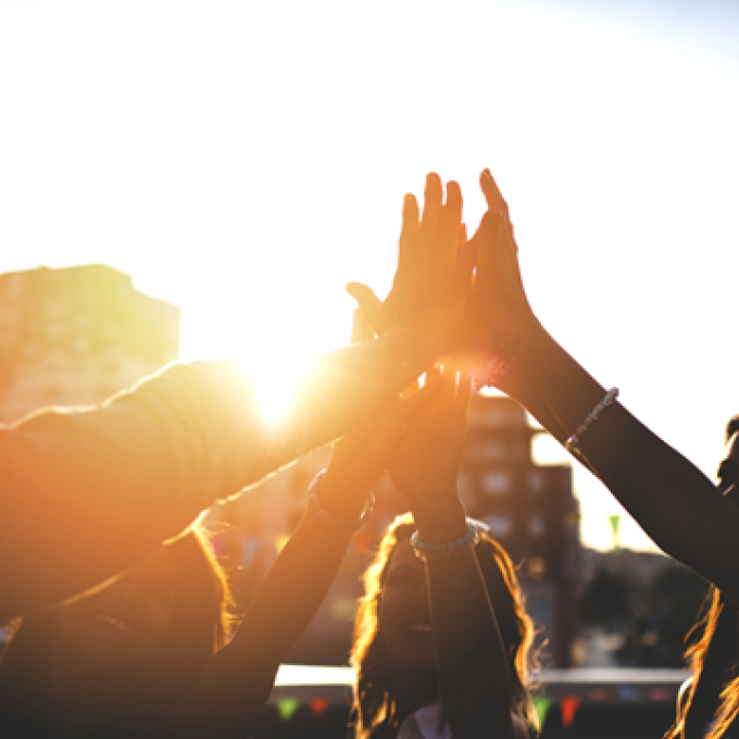 Group of people doing a high-five in sunlight.