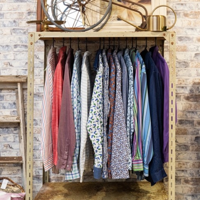 Rack of colorful patterned shirts hanging on display against a brick wall.